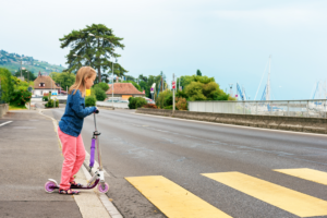 little girl crossing the street on a scooter